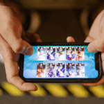 "Sepasang tangan memegang smartphone menampilkan layar game Mobile Legends Bang Bang, fokus pada tampilan kemenangan, merepresentasikan tips & trik game naik rank ML."