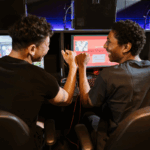 Dua gamer sedang fokus bermain di depan banyak monitor, menunjukkan intensitas dalam tren industri game.