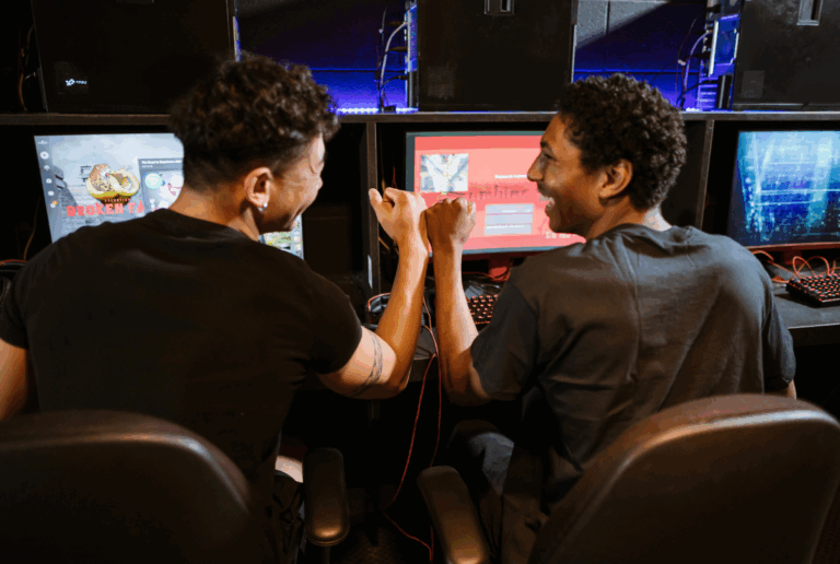 Dua gamer sedang fokus bermain di depan banyak monitor, menunjukkan intensitas dalam tren industri game.