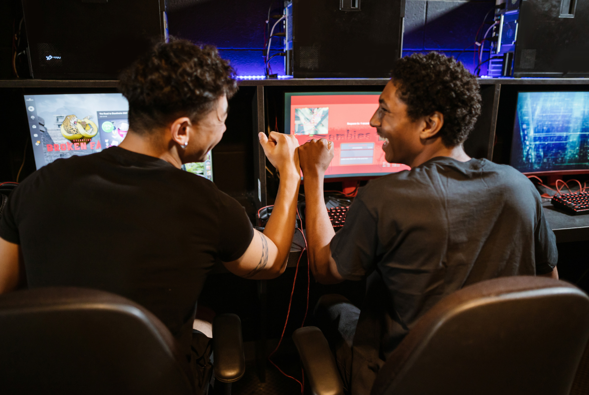 Dua gamer sedang fokus bermain di depan banyak monitor, menunjukkan intensitas dalam tren industri game.